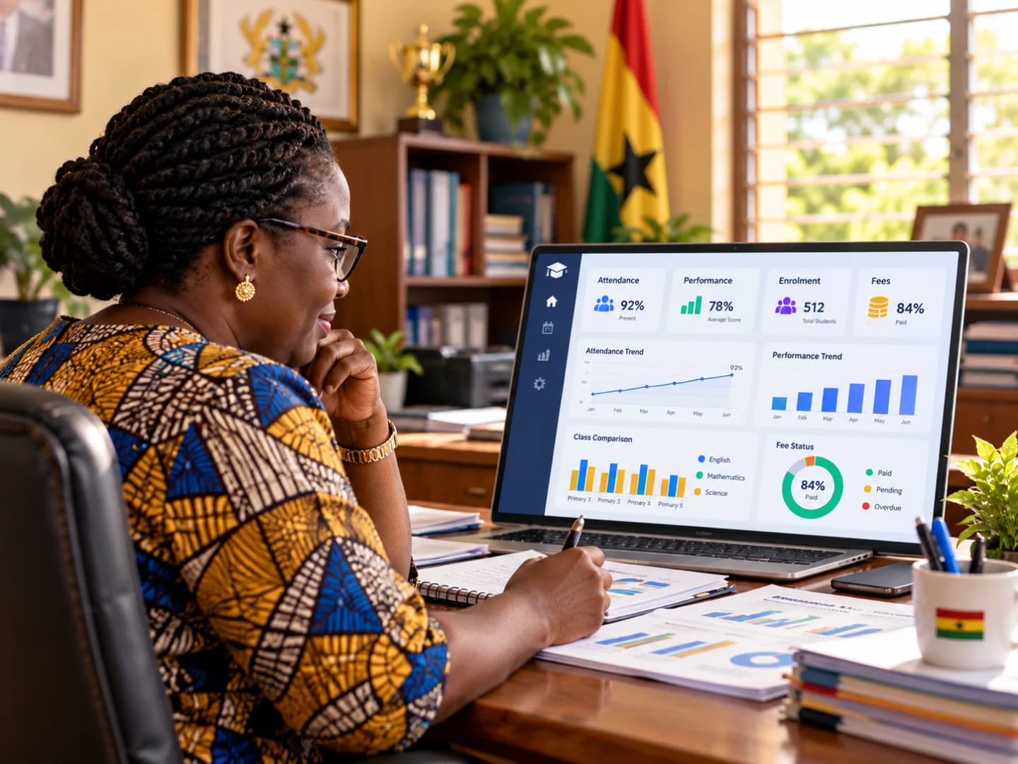 Illustration of an education professional in a patterned dress reviewing a laptop dashboard of attendance, performance, enrolment and fee figures, with printed charts on the desk and a Ghana flag in the office.